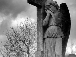 Black and white headstone showing an angel on a cross in old section