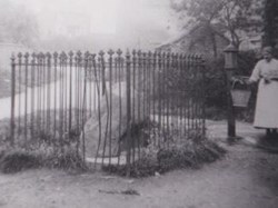 The boulder at the bottom of the hill. Said to have been found in a ditch at the top of the hill. The iron railings were removed during the war to make armaments. One of the village pumps is in the background