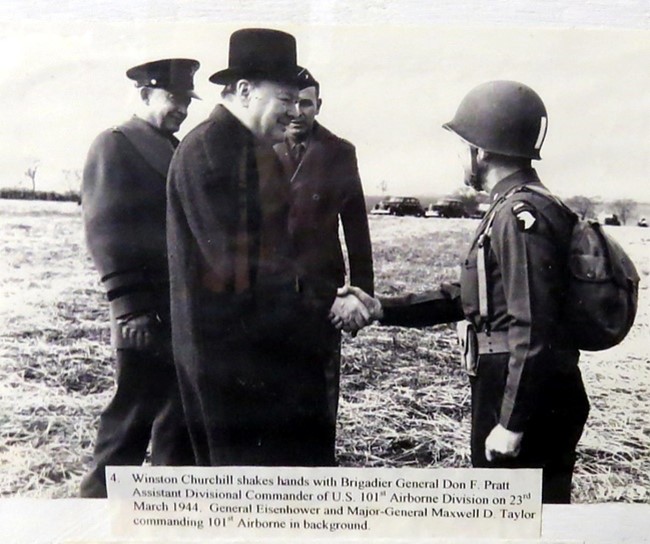 Winston Churchill shakes hands with Brigadier General Don F. Pratt, 23rd March 1944. General Eisenhower and Major-General Maxwell D. Taylor commanding 101st Airborne in background.