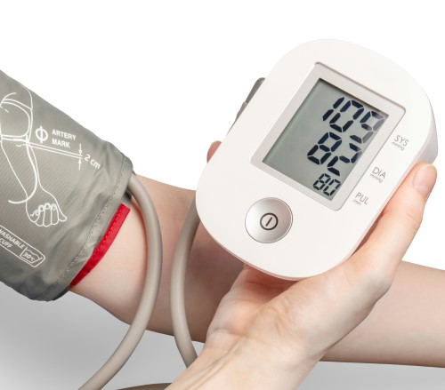 Close up of a white person wearing a blood pressure cuff on their arm and checking a hand-held blood pressure monitor, by Mockup Graphics on Unsplash