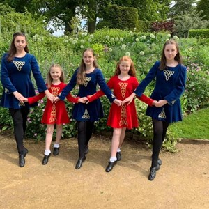 Four of the Blackrock Irish Dancers in their red and dark blue dresses linking hands ready to dance