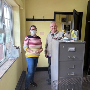 Volunteers Maria & Cliff with the previous wall colour, carpet tiles and cluttered room at start of update