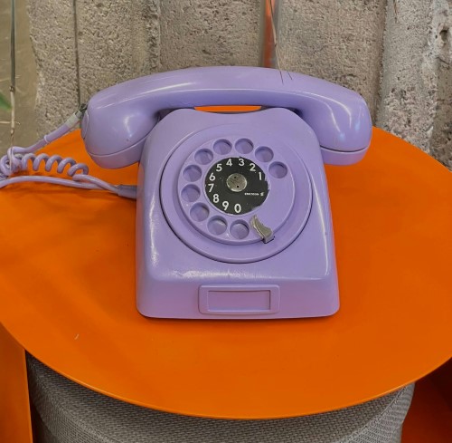 Photo of a lilac coloured landline telephone on an orange side table. Photo by Nadia Rudenko on Unsplash
