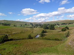 Looking back across the rolling hills to Malham Cove just right of centre.